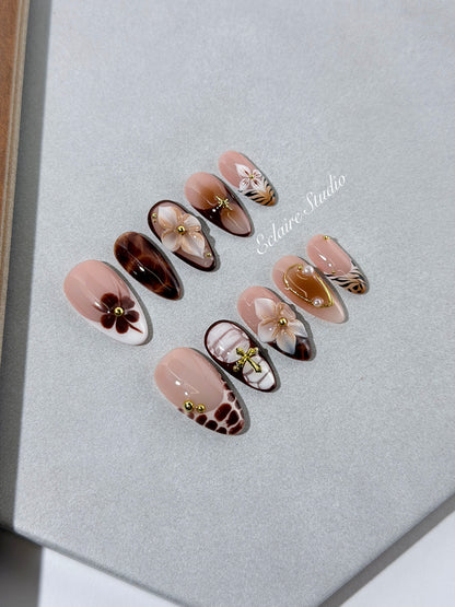 Petal Locket almond press-on nails with nude bases, ivory 3D flowers, brown florals, tortoiseshell, animal-print French tips, pearls, and gold accents.
