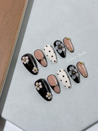 Cocoa Cameo almond press-on nails with espresso and blush bases, brown polka dots on ivory, sculpted flowers, pink daisies, and gold beads.
