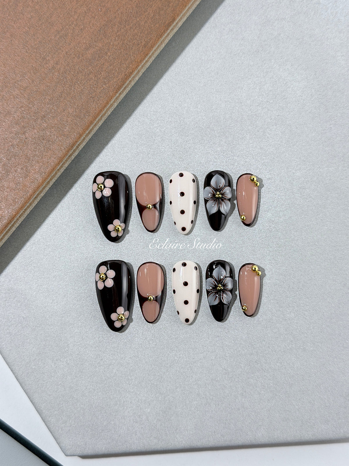 Cocoa Cameo almond press-on nails with espresso and blush bases, brown polka dots on ivory, sculpted flowers, pink daisies, and gold beads.