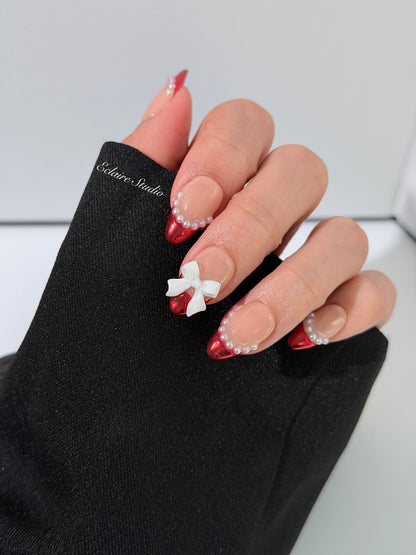 Red Ribbon press-on nails with glazed red chrome French tips, pearl trim, and 3D white bow accents.”