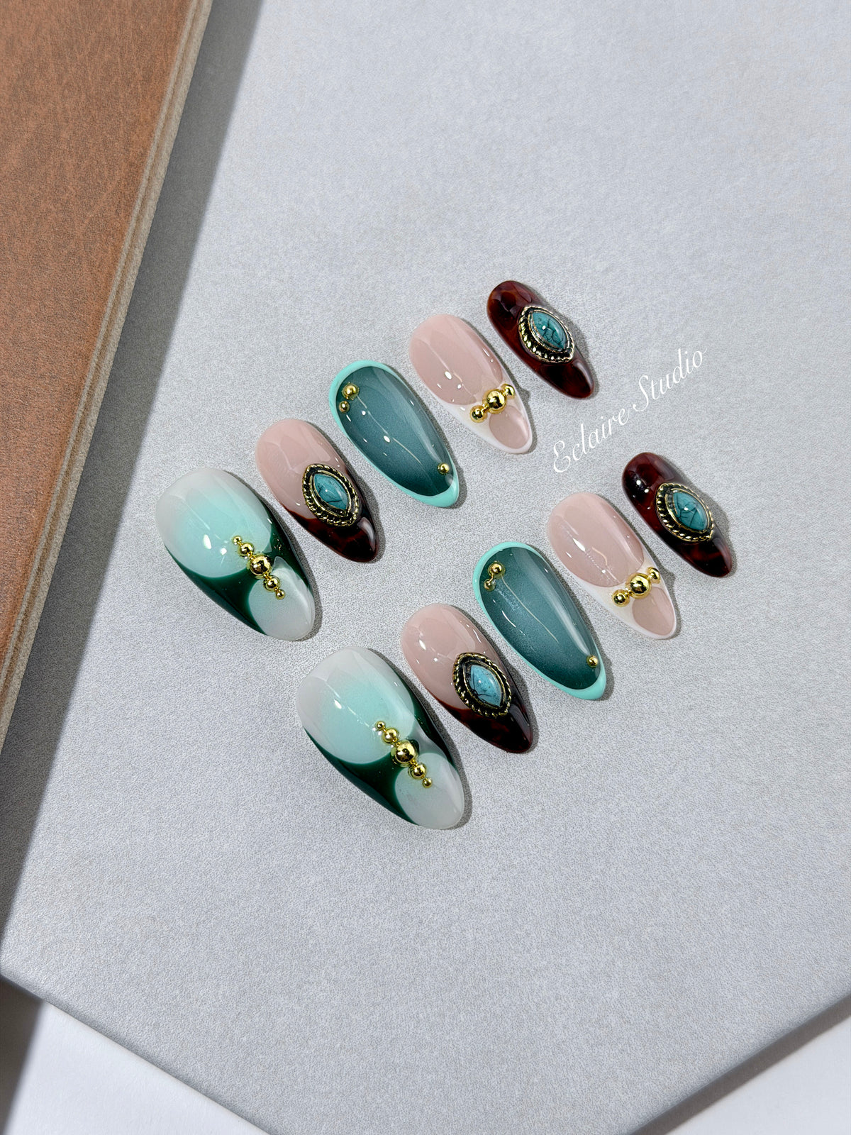 Jasmine’s Secret almond press-on nails with teal and blush bases, tortoiseshell French tips, turquoise-toned oval jewels, gold frames, and gold beads.