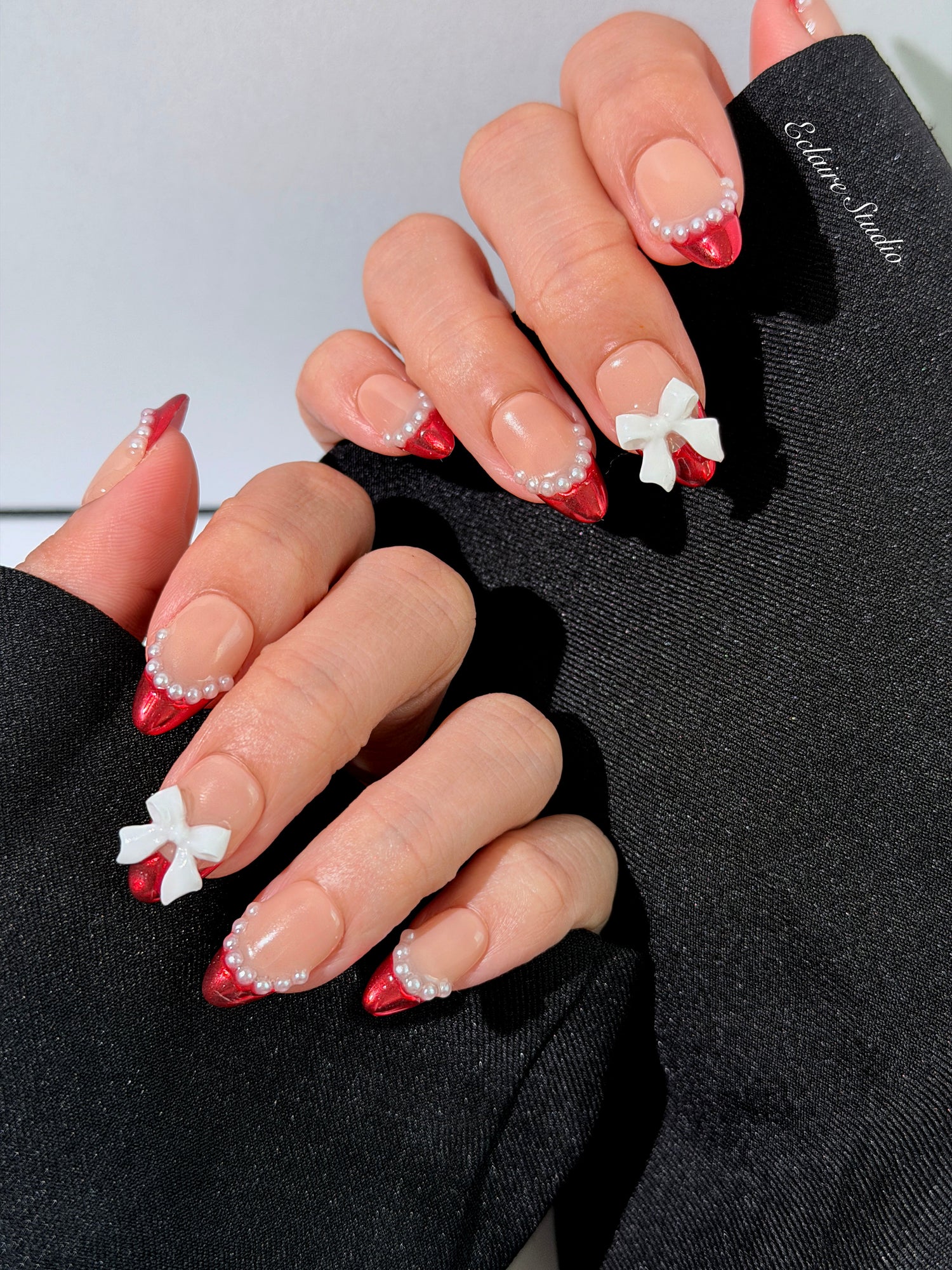 Red Ribbon press-on nails with glazed red chrome French tips, pearl trim, and 3D white bow accents.”