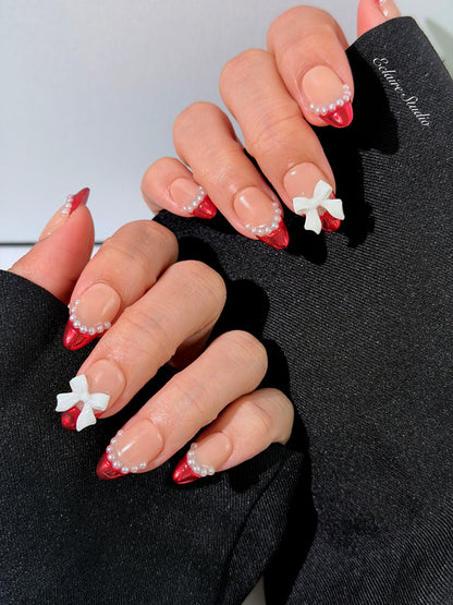 Red Ribbon press-on nails with glazed red chrome French tips, pearl trim, and 3D white bow accents.”