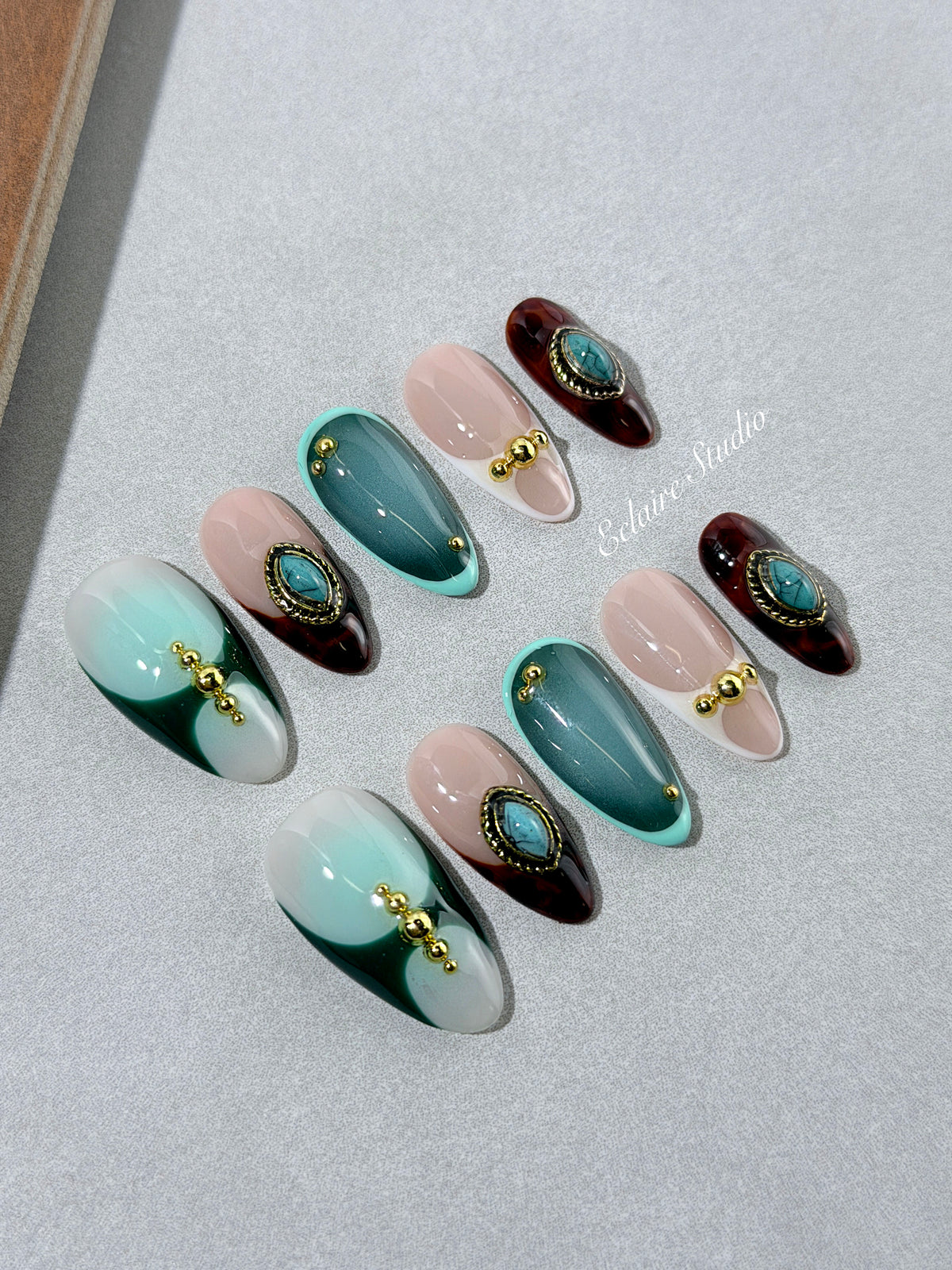Jasmine’s Secret almond press-on nails with teal and blush bases, tortoiseshell French tips, turquoise-toned oval jewels, gold frames, and gold beads.