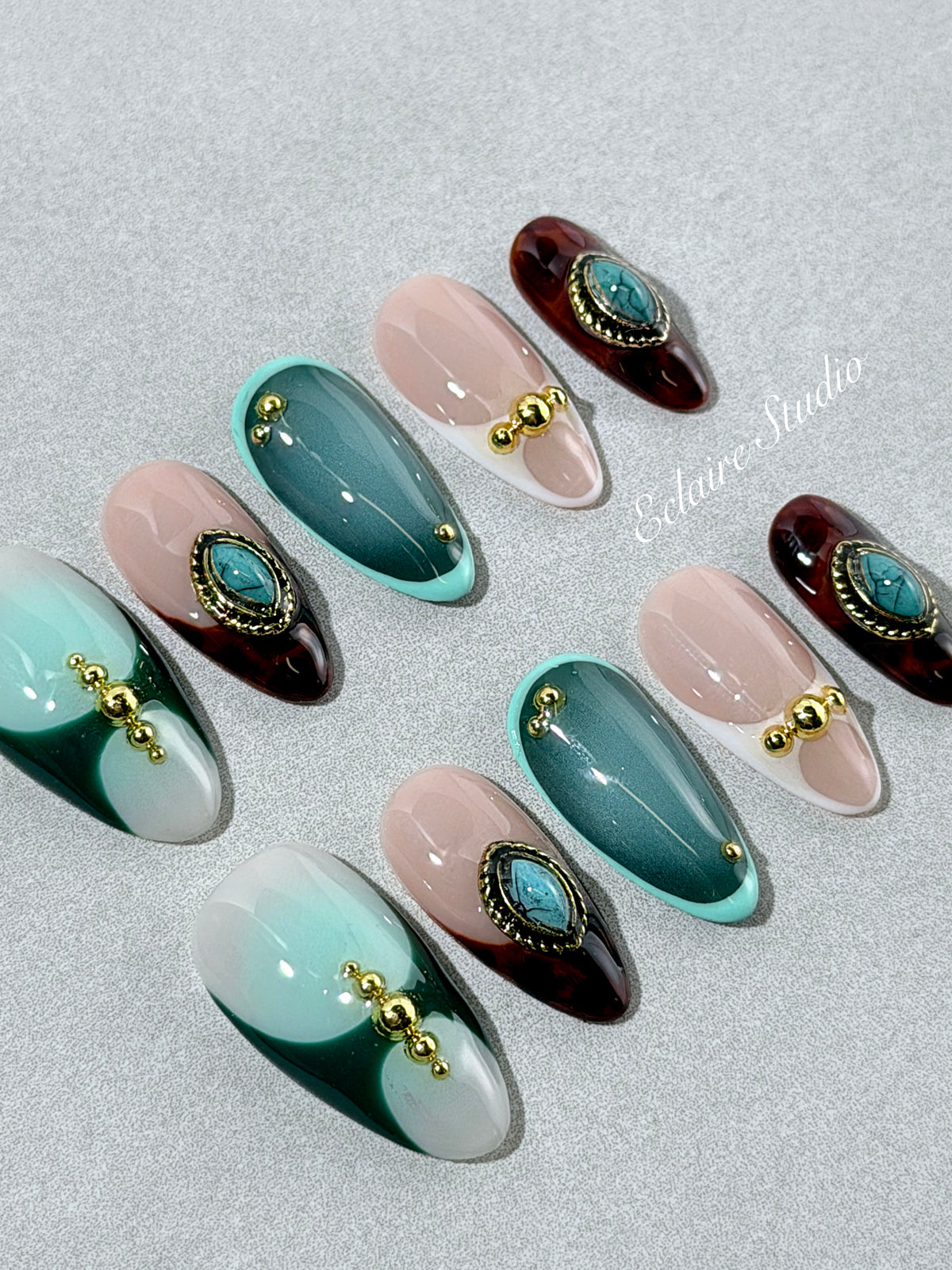Jasmine’s Secret almond press-on nails with teal and blush bases, tortoiseshell French tips, turquoise-toned oval jewels, gold frames, and gold beads.