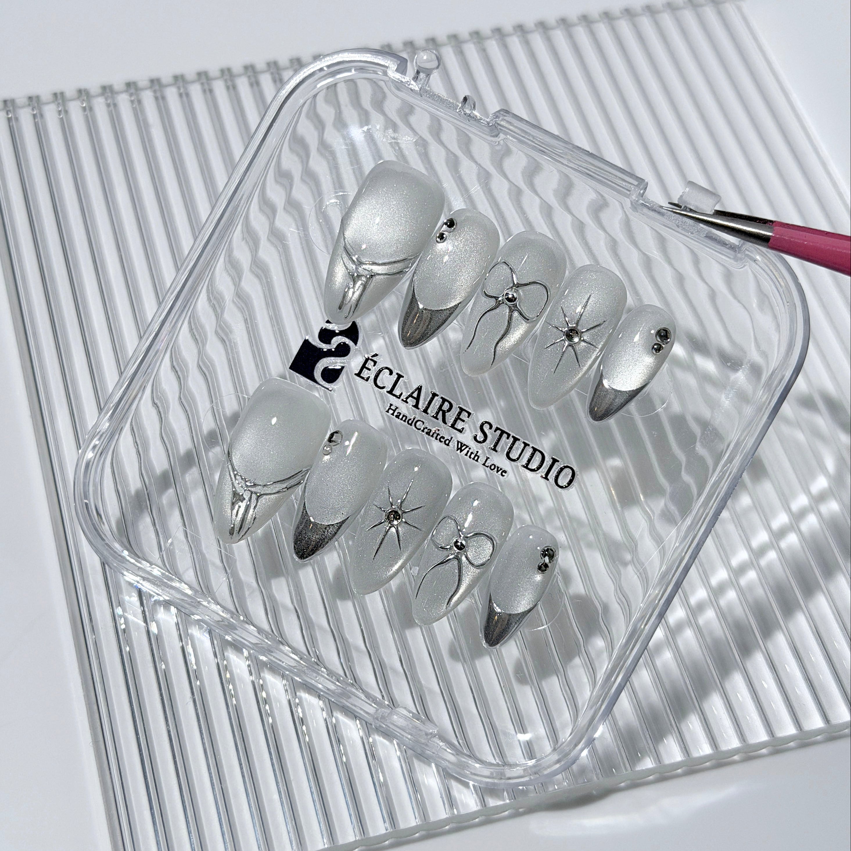 Silver cat-eye press-on nails featuring glazed chrome French tips and fine-line bow and starburst designs.