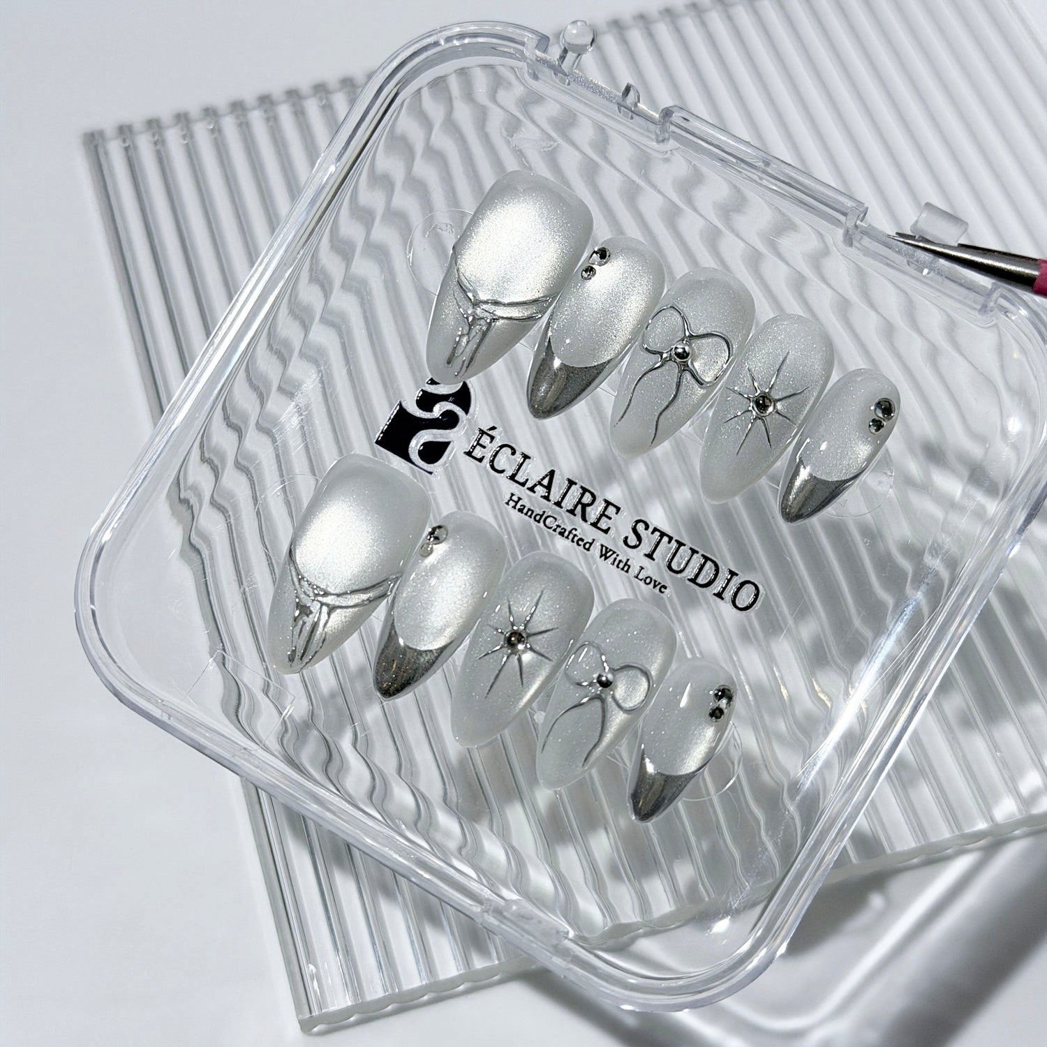 Silver cat-eye press-on nails featuring glazed chrome French tips and fine-line bow and starburst designs.