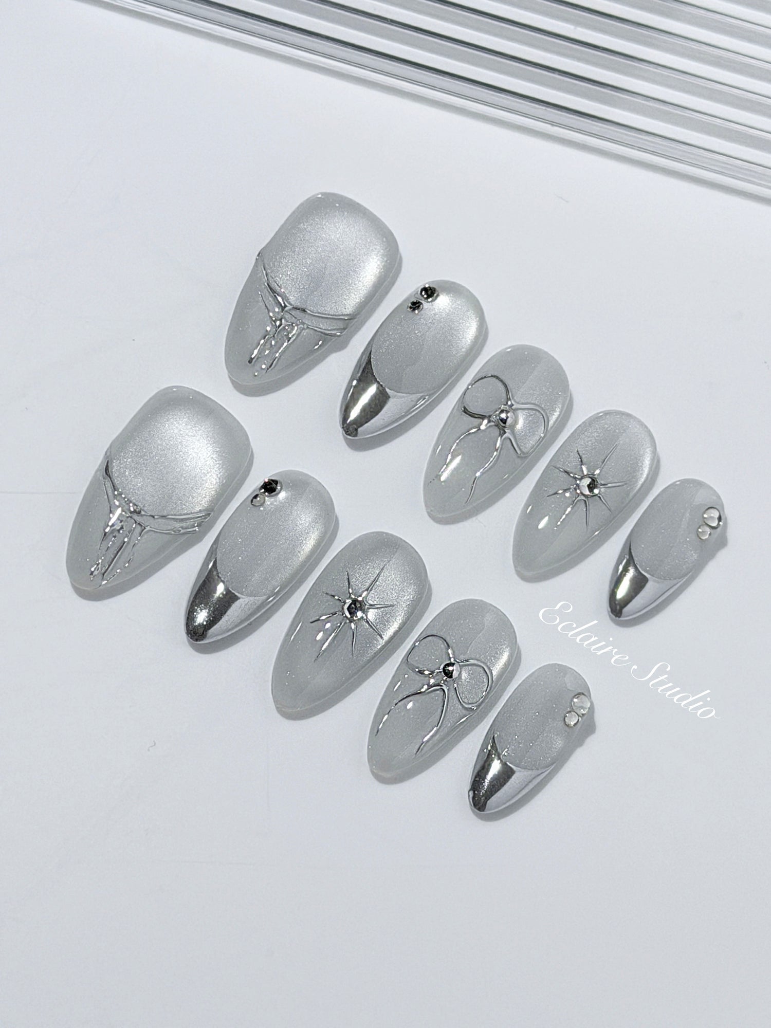Silver cat-eye press-on nails featuring glazed chrome French tips and fine-line bow and starburst designs.
