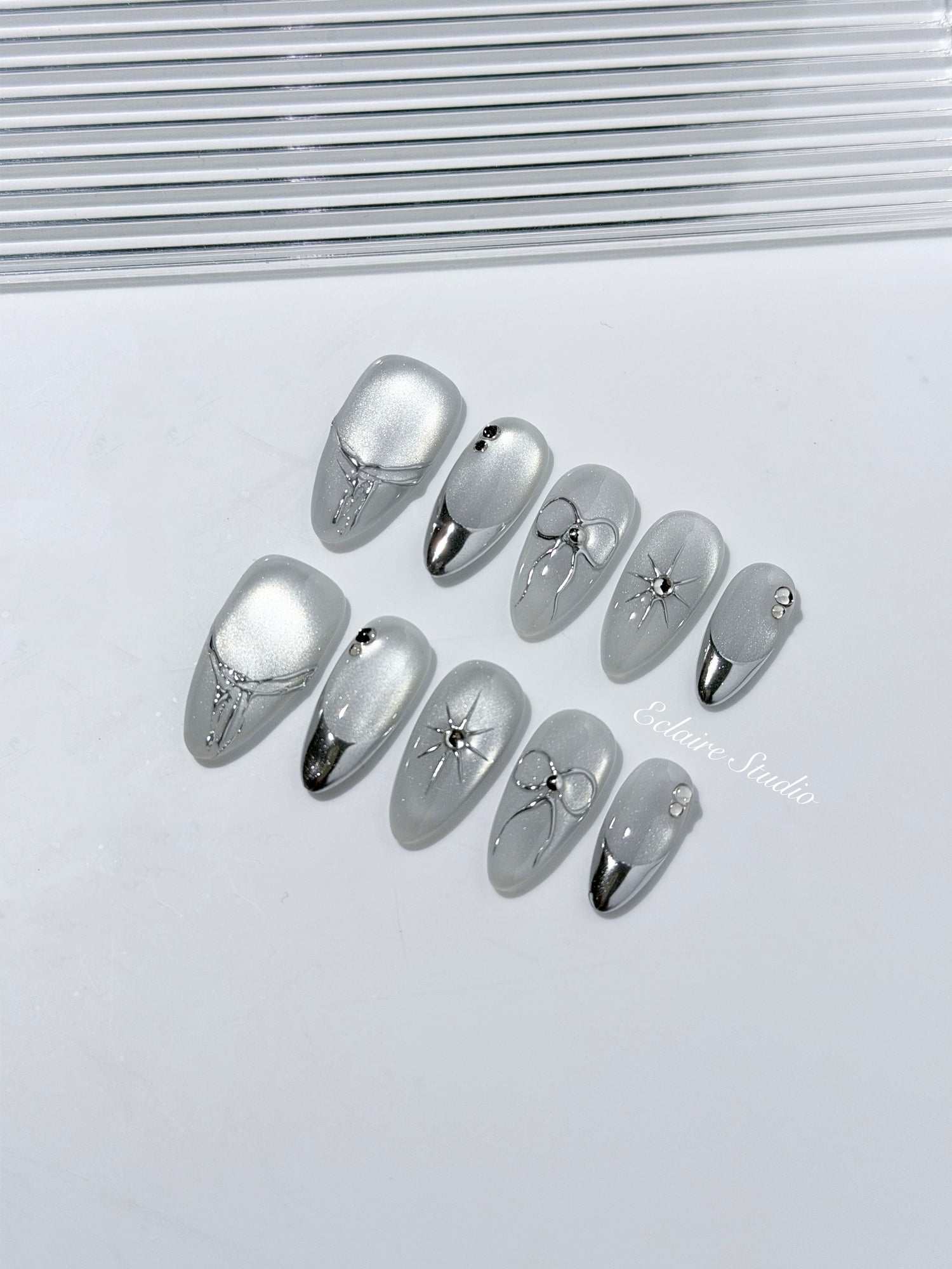 Silver cat-eye press-on nails featuring glazed chrome French tips and fine-line bow and starburst designs.