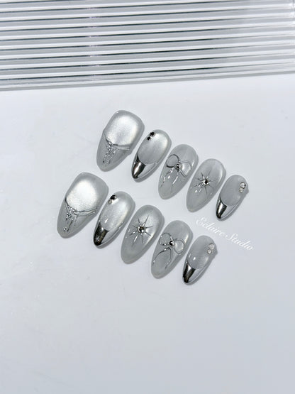 Silver cat-eye press-on nails featuring glazed chrome French tips and fine-line bow and starburst designs.