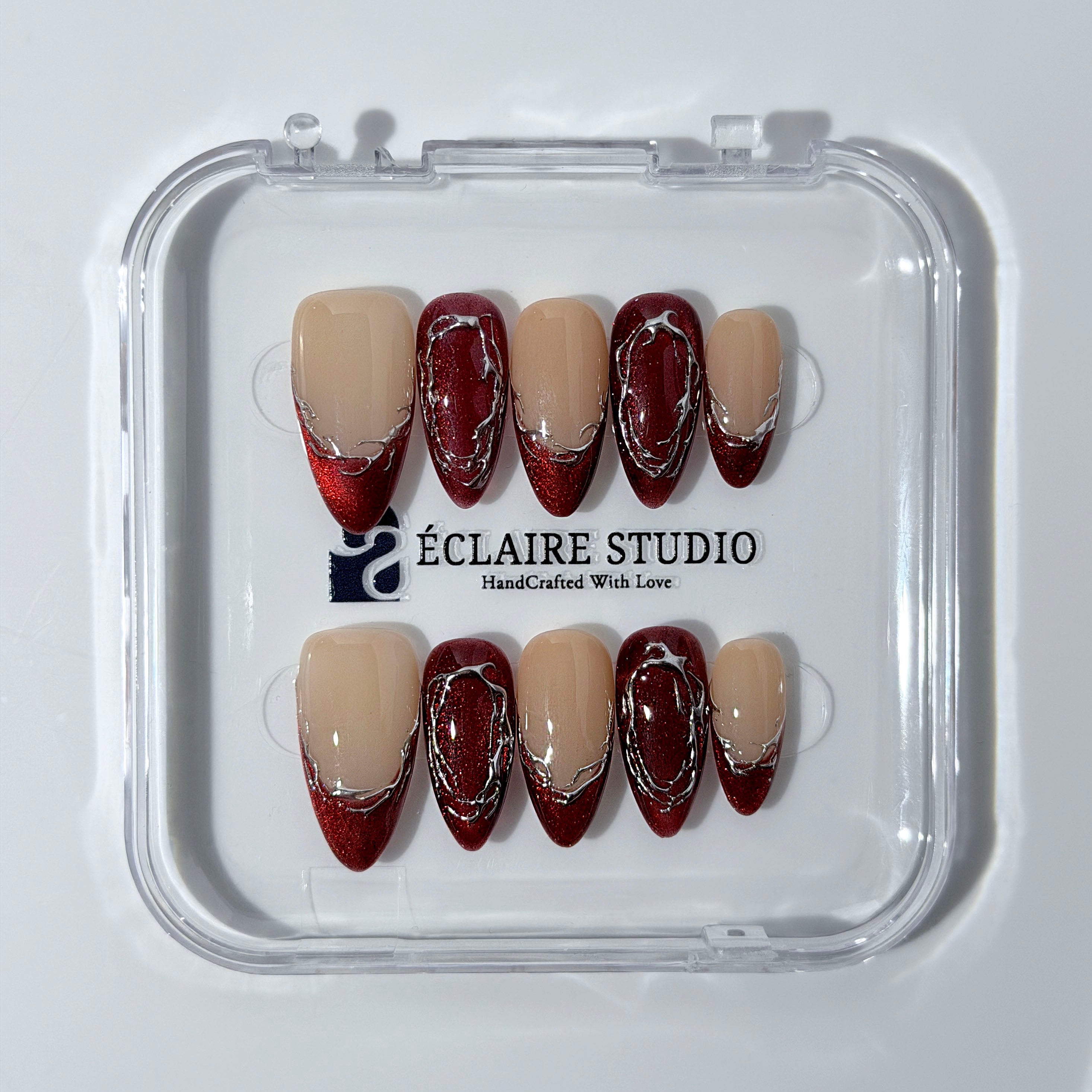 Red press-on nails with deep red cat-eye base, silver strokes, and nude contrast — Éclaire Nail Studio