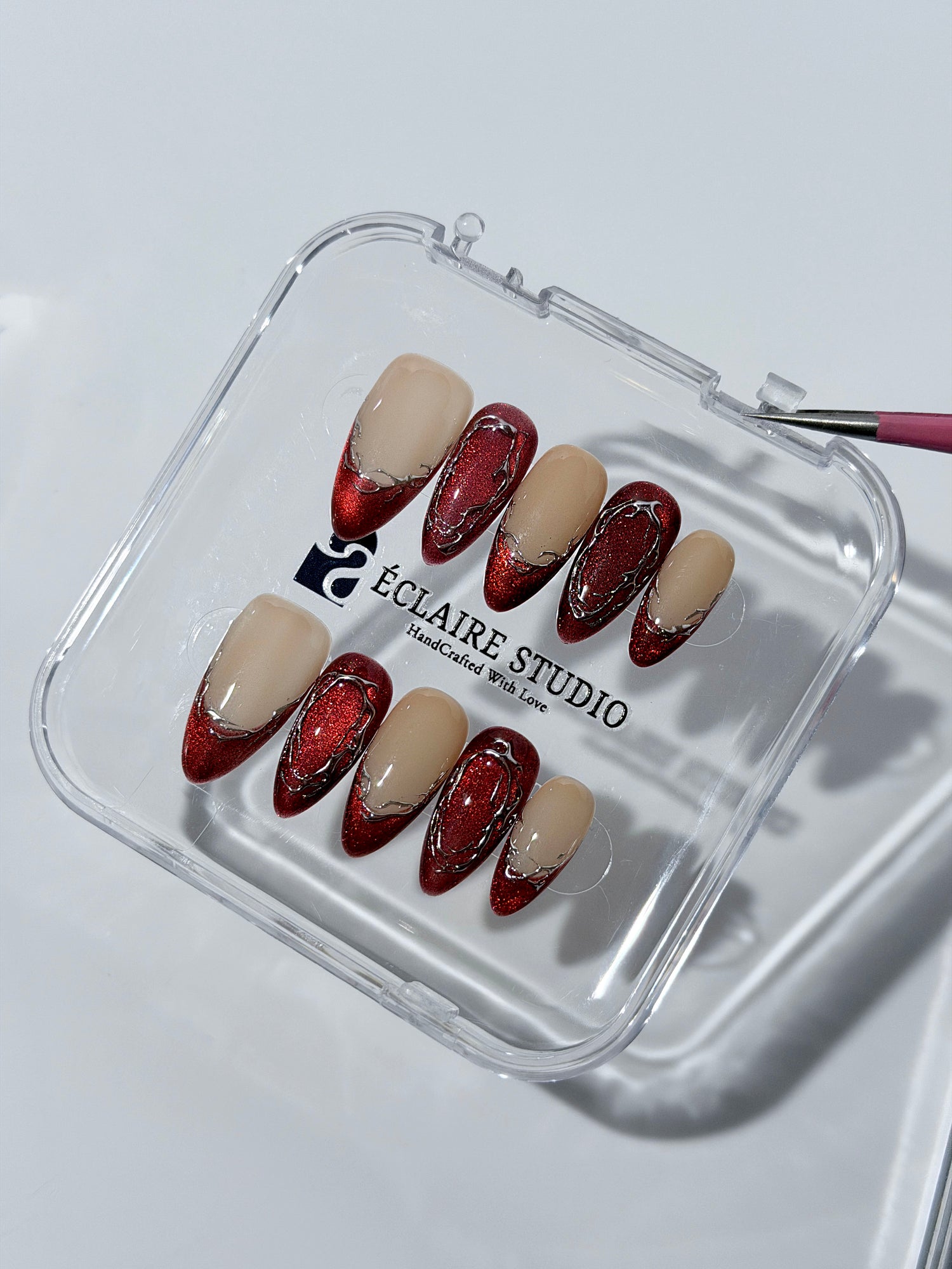 Red press-on nails with deep red cat-eye base, silver strokes, and nude contrast — Éclaire Nail Studio