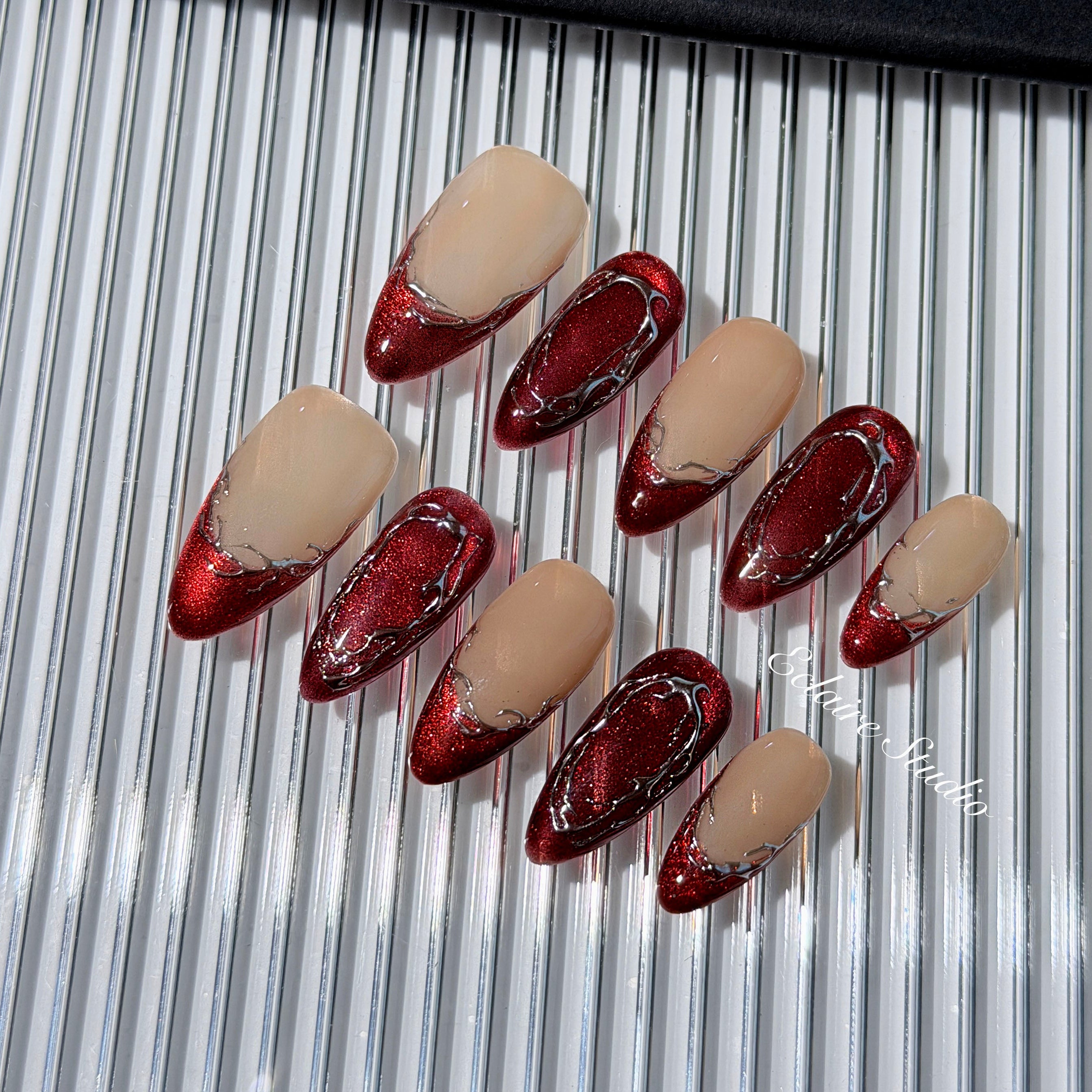 Red press-on nails with deep red cat-eye base, silver strokes, and nude contrast — Éclaire Nail Studio