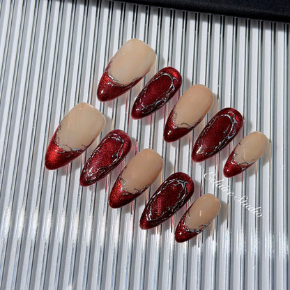 Red press-on nails with deep red cat-eye base, silver strokes, and nude contrast — Éclaire Nail Studio