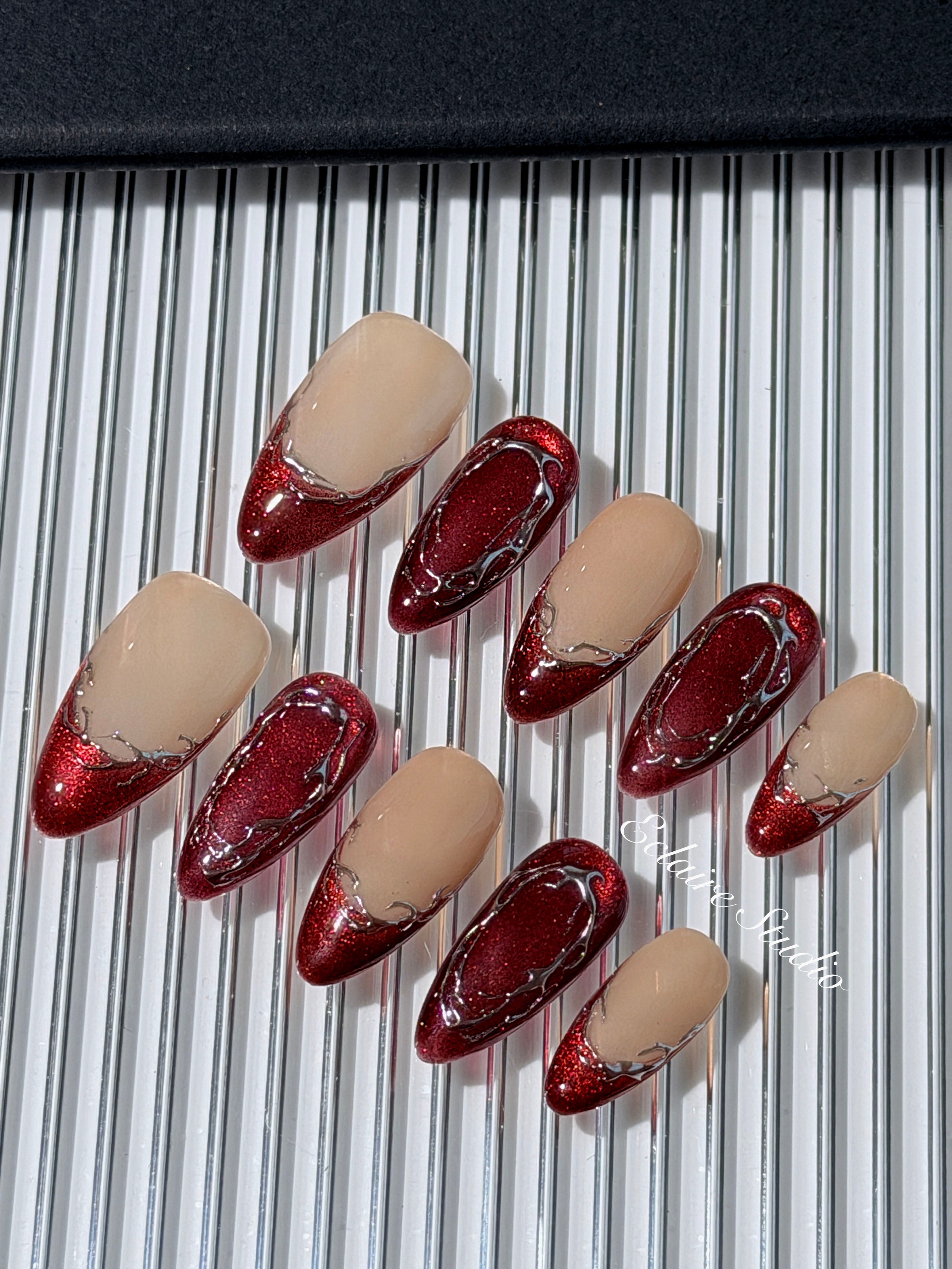Red press-on nails with deep red cat-eye base, silver strokes, and nude contrast — Éclaire Nail Studio