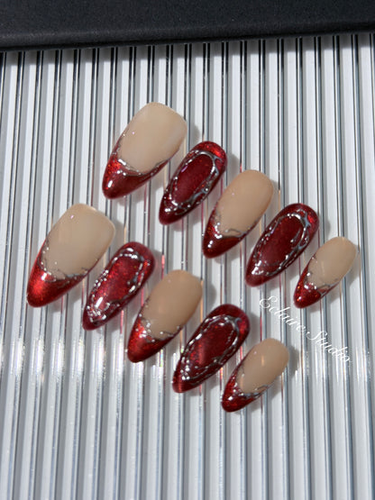 Red press-on nails with deep red cat-eye base, silver strokes, and nude contrast — Éclaire Nail Studio