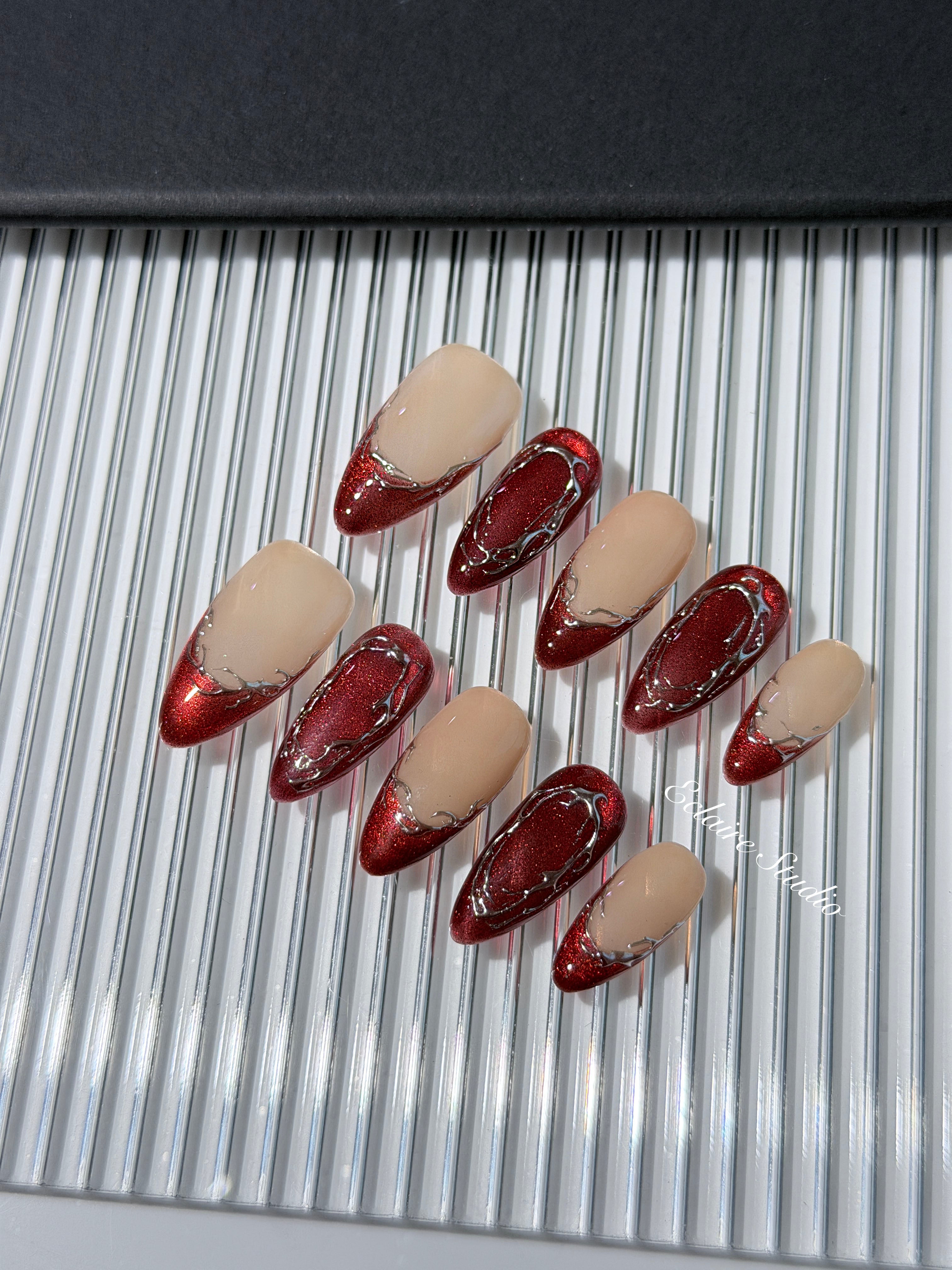 Red press-on nails with deep red cat-eye base, silver strokes, and nude contrast — Éclaire Nail Studio