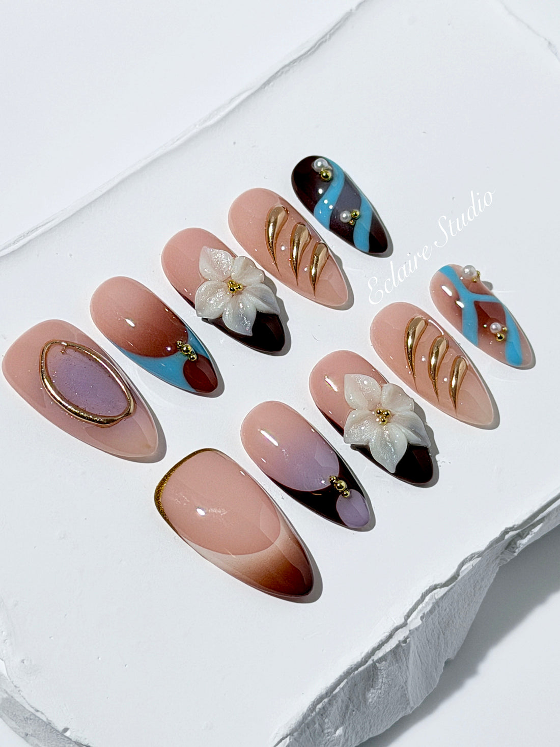 Warm gradient nails with gold trim, 3D white flowers, and blue accents inspired by the Nutcracker character