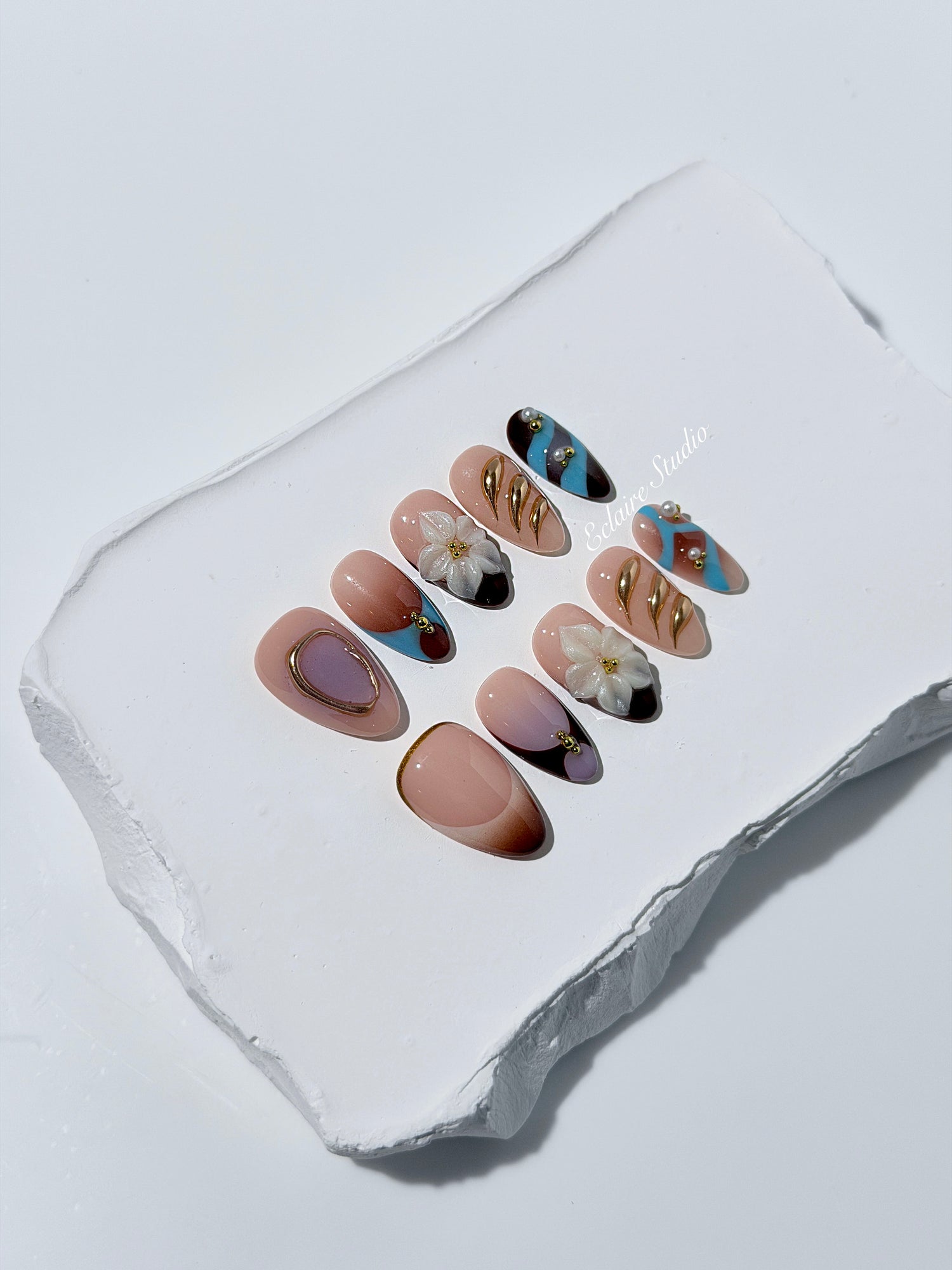 Warm gradient nails with gold trim, 3D white flowers, and blue accents inspired by the Nutcracker character