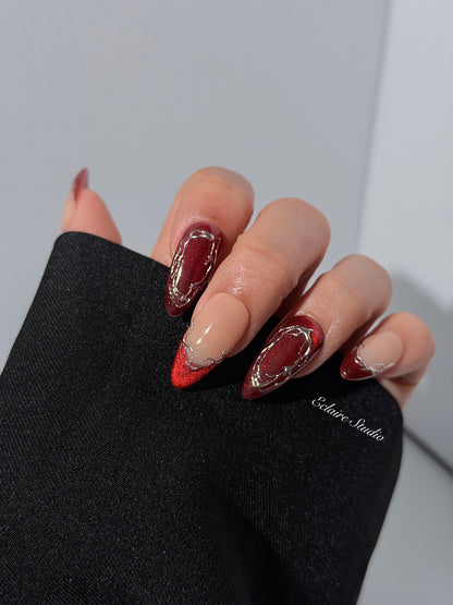 Red press-on nails with deep red cat-eye base, silver strokes, and nude contrast — Éclaire Nail Studio