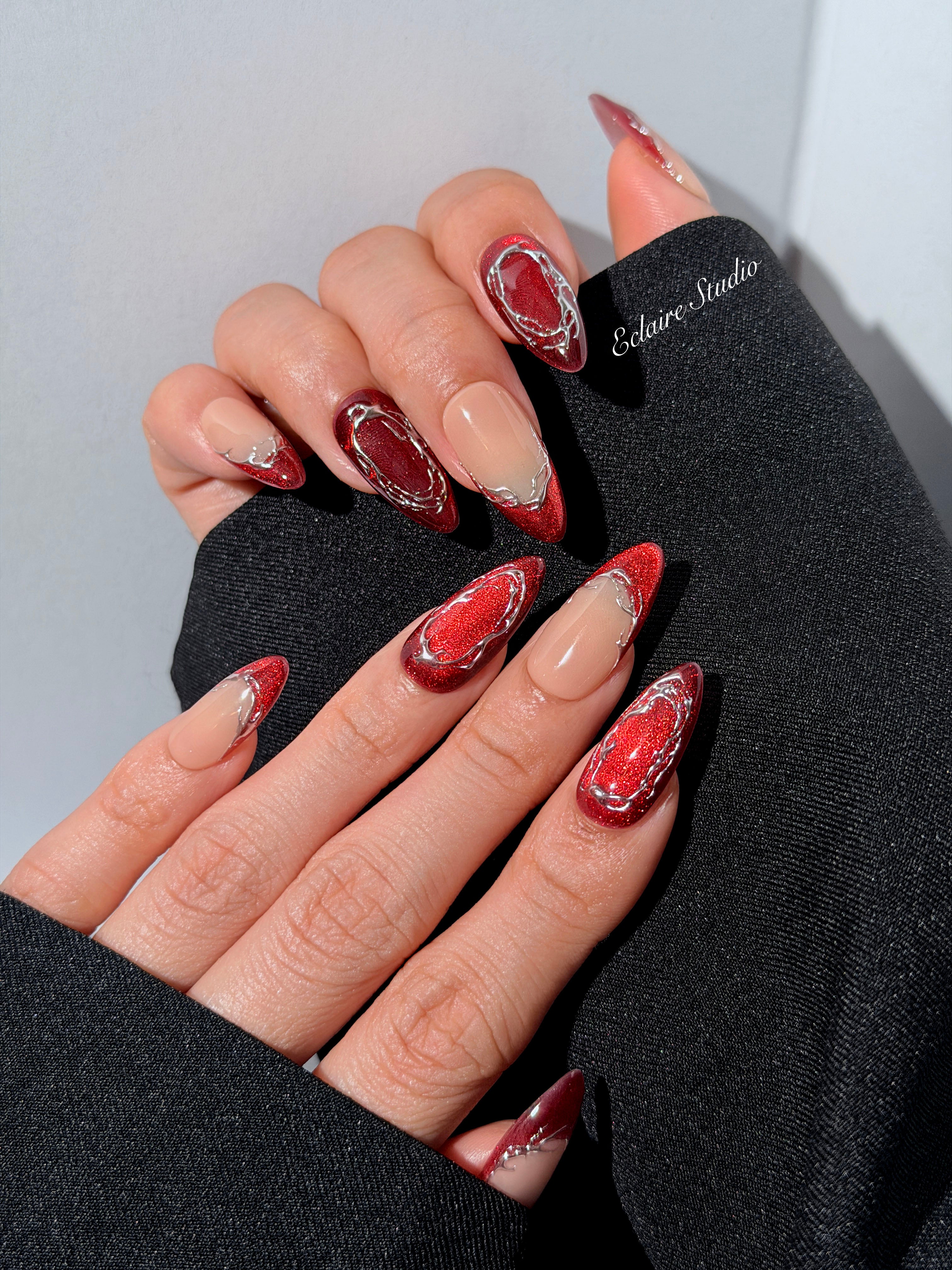 Red press-on nails with deep red cat-eye base, silver strokes, and nude contrast — Éclaire Nail Studio