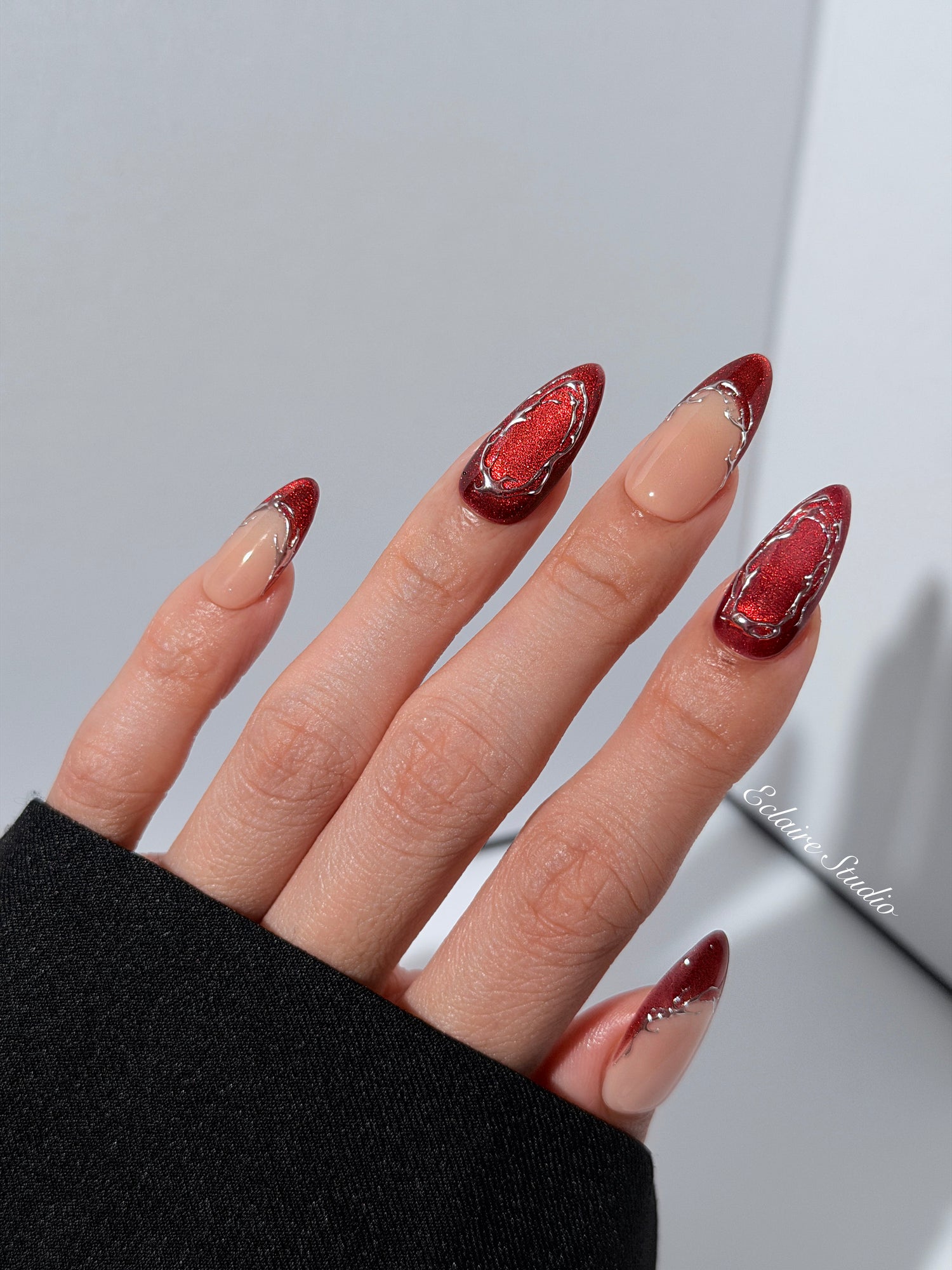 Red press-on nails with deep red cat-eye base, silver strokes, and nude contrast — Éclaire Nail Studio