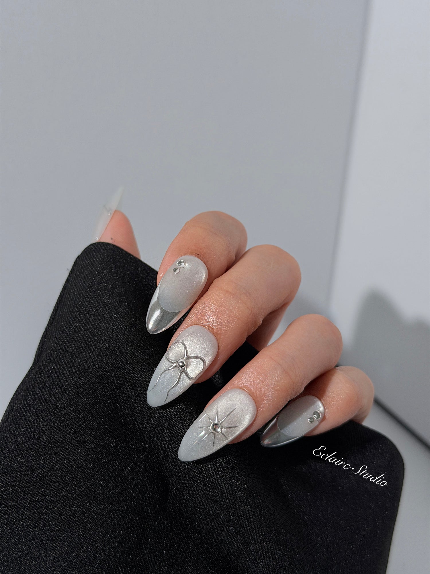 Silver cat-eye press-on nails featuring glazed chrome French tips and fine-line bow and starburst designs.