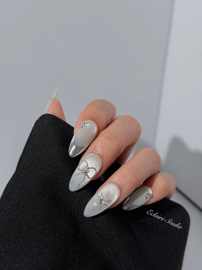 Silver cat-eye press-on nails featuring glazed chrome French tips and fine-line bow and starburst designs.
