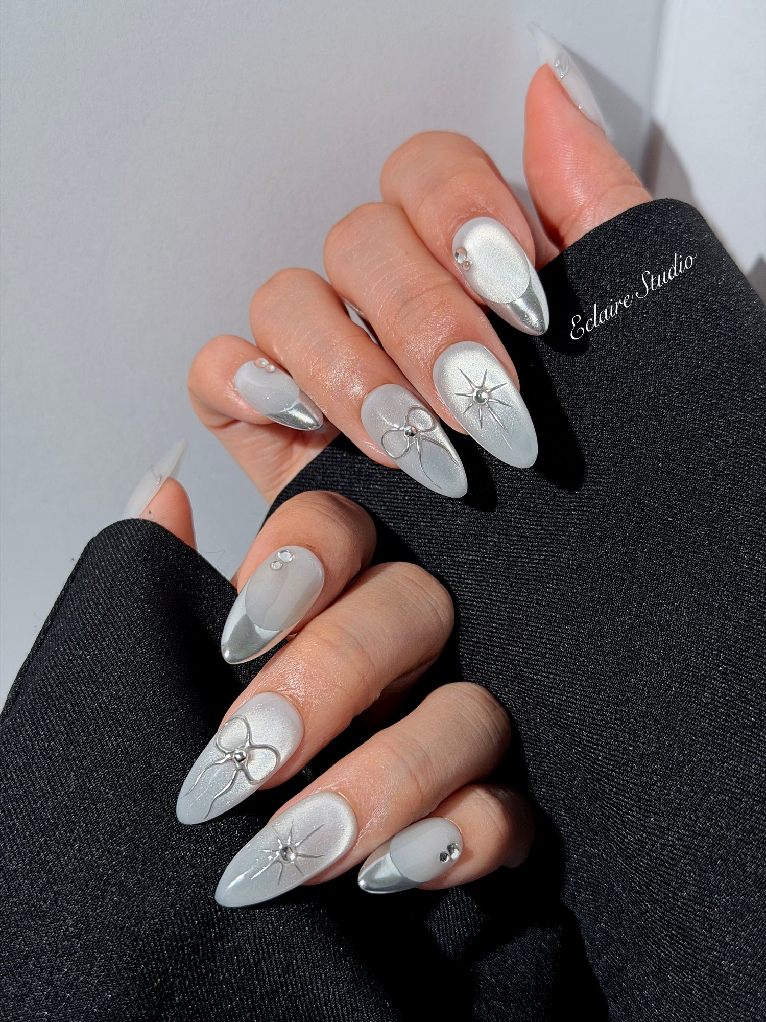 Silver cat-eye press-on nails featuring glazed chrome French tips and fine-line bow and starburst designs.