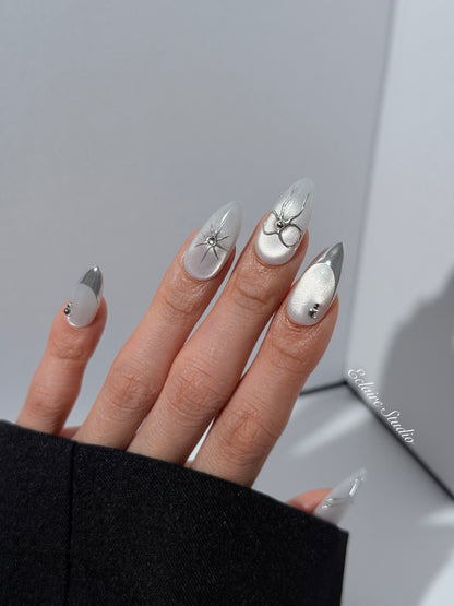 Silver cat-eye press-on nails featuring glazed chrome French tips and fine-line bow and starburst designs.