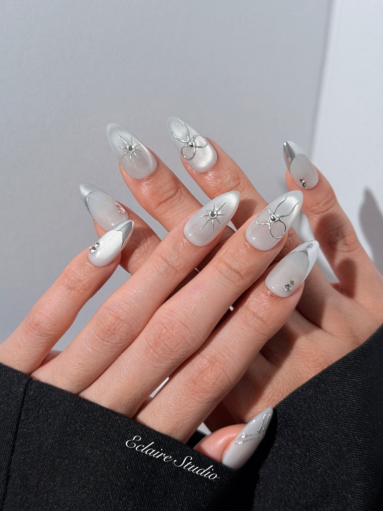 Silver cat-eye press-on nails featuring glazed chrome French tips and fine-line bow and starburst designs.
