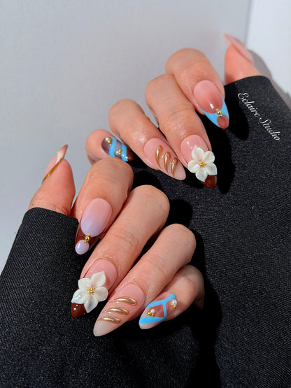 Warm gradient nails with gold trim, 3D white flowers, and blue accents inspired by the Nutcracker character