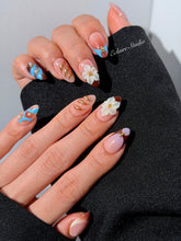 Warm gradient nails with gold trim, 3D white flowers, and blue accents inspired by the Nutcracker character