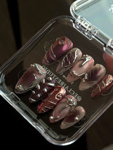 Set of long, almond-shaped press-on nails with a pink-to-purple multichrome base, accented by sculpted chrome designs, metallic textures, and small silver studs, displayed on a ribbed reflective surface under natural light.