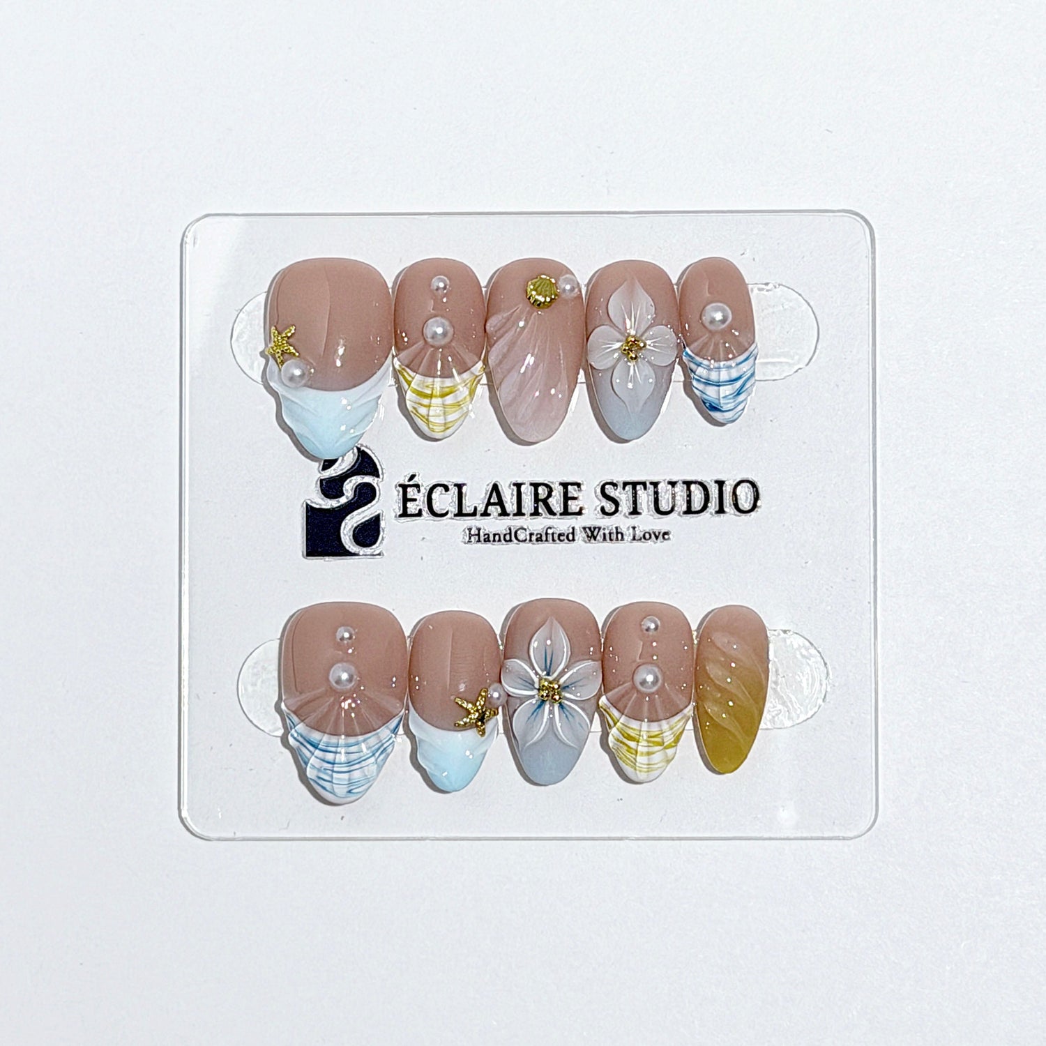 Artisanal resort-style press-on nails with a sheer nude base, pastel blue and yellow striped French tips, 3D sculpted flowers, and gold starfish charms with mini pearls.