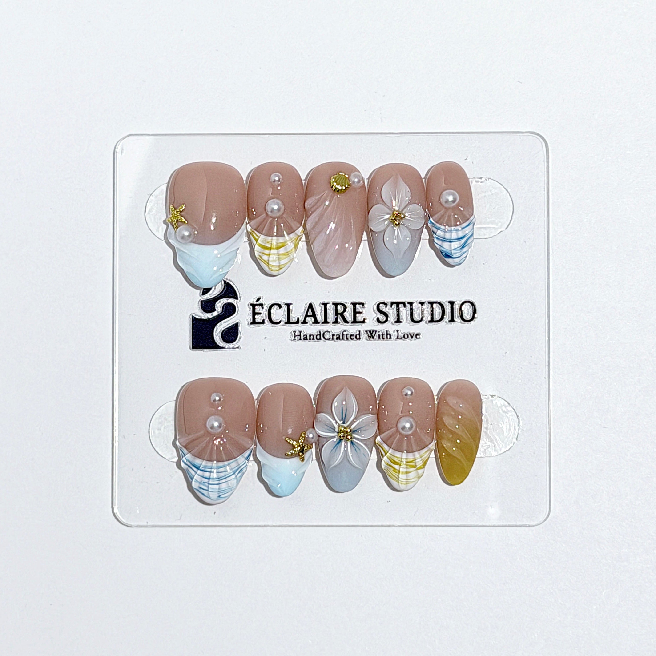 Artisanal resort-style press-on nails with a sheer nude base, pastel blue and yellow striped French tips, 3D sculpted flowers, and gold starfish charms with mini pearls.