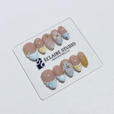 Artisanal resort-style press-on nails with a sheer nude base, pastel blue and yellow striped French tips, 3D sculpted flowers, and gold starfish charms with mini pearls.
