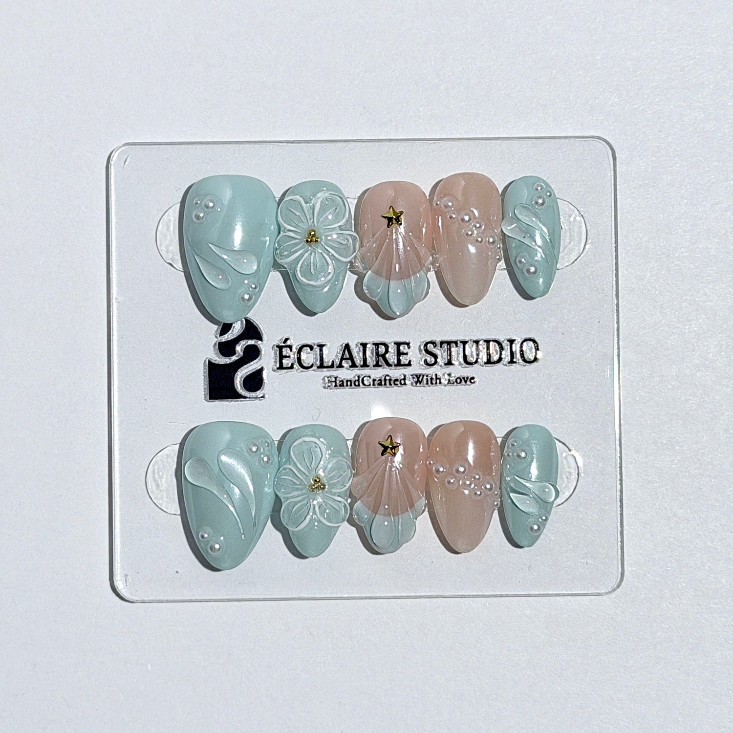 Eclaire Nail Studio 3D Summer short almond press-on nails featuring a light aqua glazed base and peachy-nude accent nails with 3D sculpted ocean waves, 3D flowers, and seashell tips with mini pearls and gold stars.