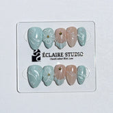 Eclaire Nail Studio 3D Summer short almond press-on nails featuring a light aqua glazed base and peachy-nude accent nails with 3D sculpted ocean waves, 3D flowers, and seashell tips with mini pearls and gold stars.