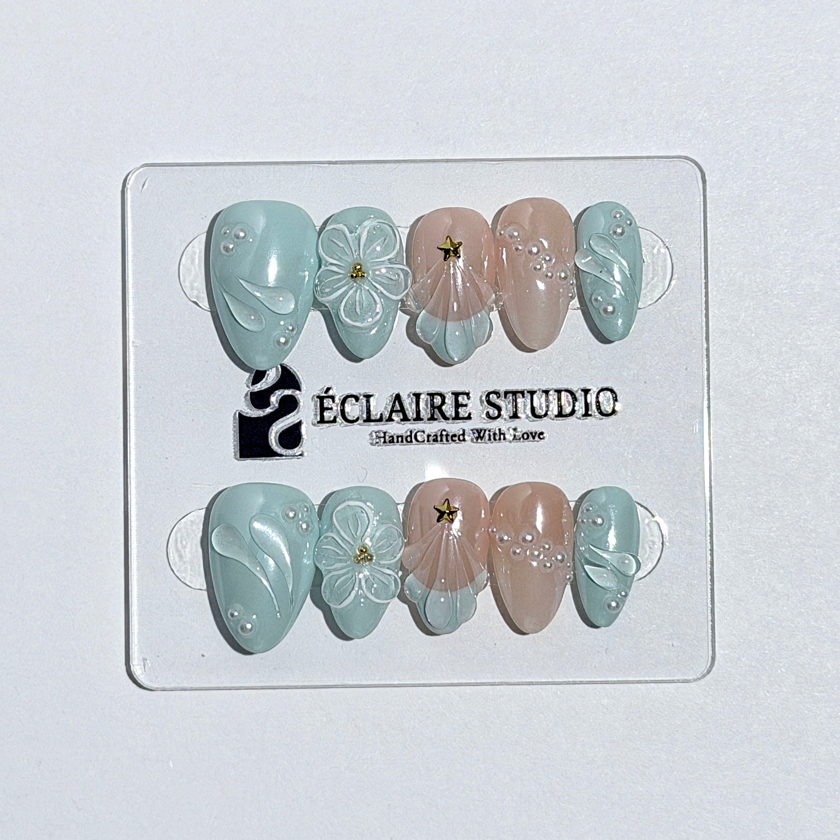 Eclaire Nail Studio 3D Summer short almond press-on nails featuring a light aqua glazed base and peachy-nude accent nails with 3D sculpted ocean waves, 3D flowers, and seashell tips with mini pearls and gold stars.