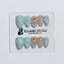 Eclaire Nail Studio 3D Summer short almond press-on nails featuring a light aqua glazed base and peachy-nude accent nails with 3D sculpted ocean waves, 3D flowers, and seashell tips with mini pearls and gold stars.