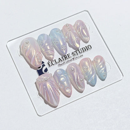 Handcrafted luxury press-on nails in a medium almond shape featuring an iridescent multi-toned glazed finish with 3D sculpted shell ridges and delicate mini pearls.