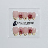 Luxury short almond press-on nails featuring sheer pink bases with vintage cream French tips, burgundy polka dots, and hand-sculpted 3D burgundy flowers with gold bead centers.