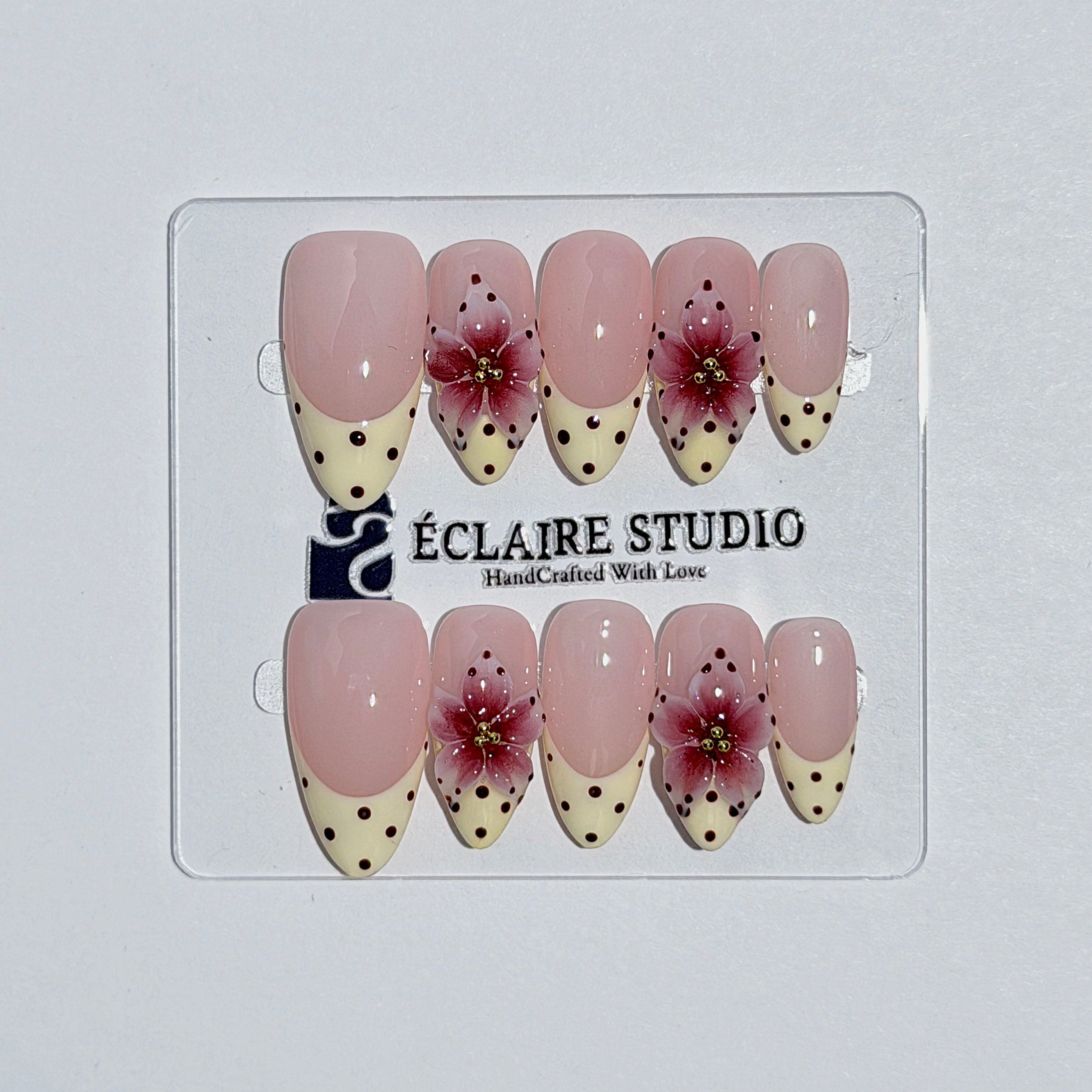 Eclaire Nail Studio Luxury medium almond press-on nails featuring sheer pink bases with vintage cream French tips, burgundy polka dots, and hand-sculpted 3D burgundy flowers with gold bead centers.
