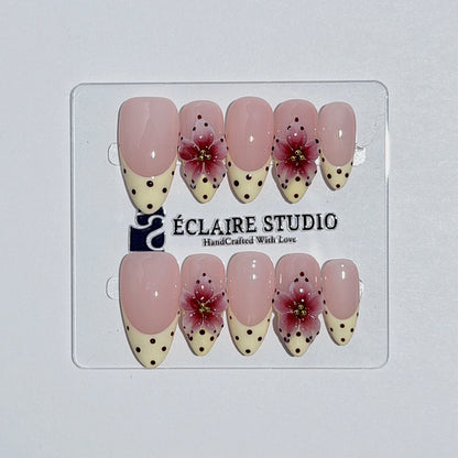 Eclaire Nail Studio Luxury medium almond press-on nails featuring sheer pink bases with vintage cream French tips, burgundy polka dots, and hand-sculpted 3D burgundy flowers with gold bead centers.