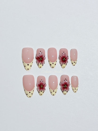 Luxury medium almond press-on nails featuring sheer pink bases with vintage cream French tips, burgundy polka dots, and hand-sculpted 3D burgundy flowers with gold bead centers.