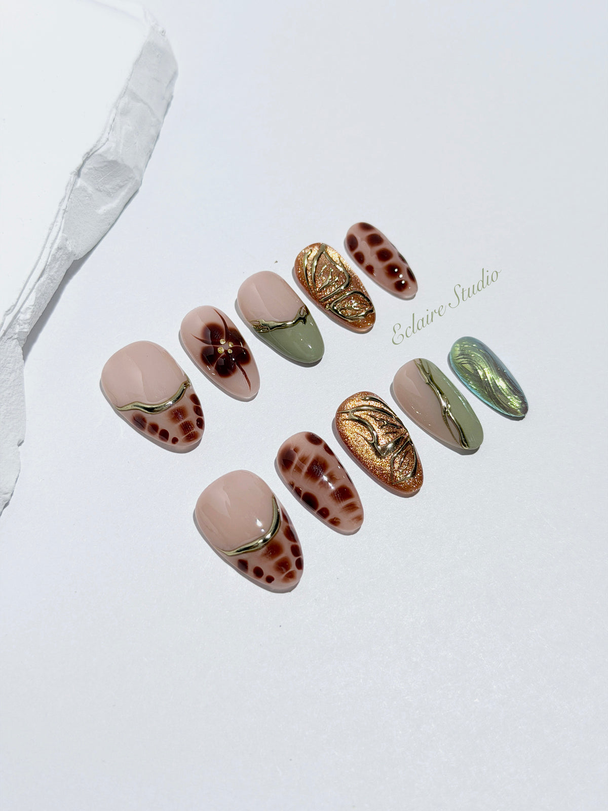 Olive Reverie short almond press-on nails with brown and green cat-eye shimmer, olive French tips, animal prints, floral art, and raised gold details.
