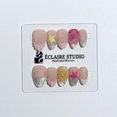 Eclaire Studio 3D Summer short almond press-on nails with sheer nude bases, sparkling silver cat-eye magnetic French tips, hand-painted colorful starfish, and pink 3D sculpted seashells.