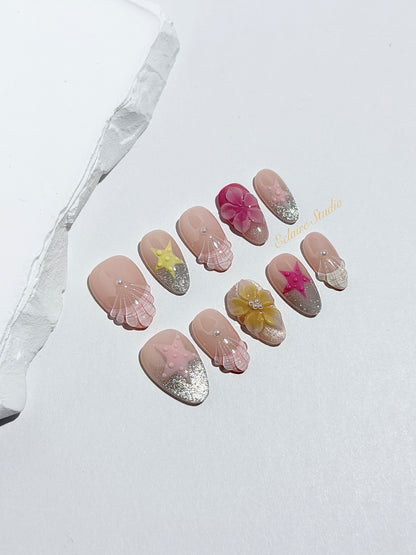 Eclaire Studio 3D Summer short almond press-on nails with sheer nude bases, sparkling silver cat-eye magnetic French tips, hand-painted colorful starfish, and pink 3D sculpted seashells.