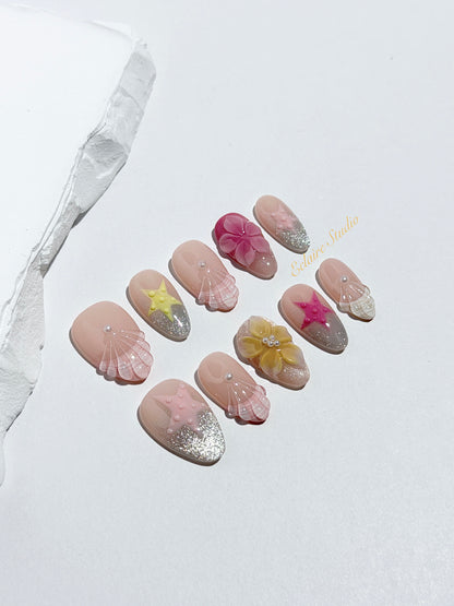 Eclaire Studio 3D Summer short almond press-on nails with sheer nude bases, sparkling silver cat-eye magnetic French tips, hand-painted colorful starfish, and pink 3D sculpted seashells.